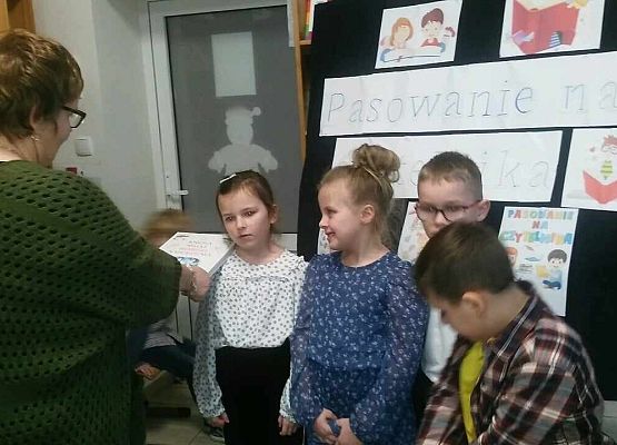 Grafika 2: "W KRÓLESTWIE KSIĄŻEK" - Pasowanie na czytelnika uczniów klasy pierwszej  w bibliotece szkolnej. NPRc 2.0